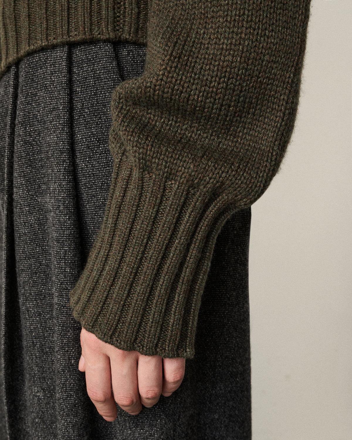 close-up of a woman's hand and cuff of the olive turtle neck sweater