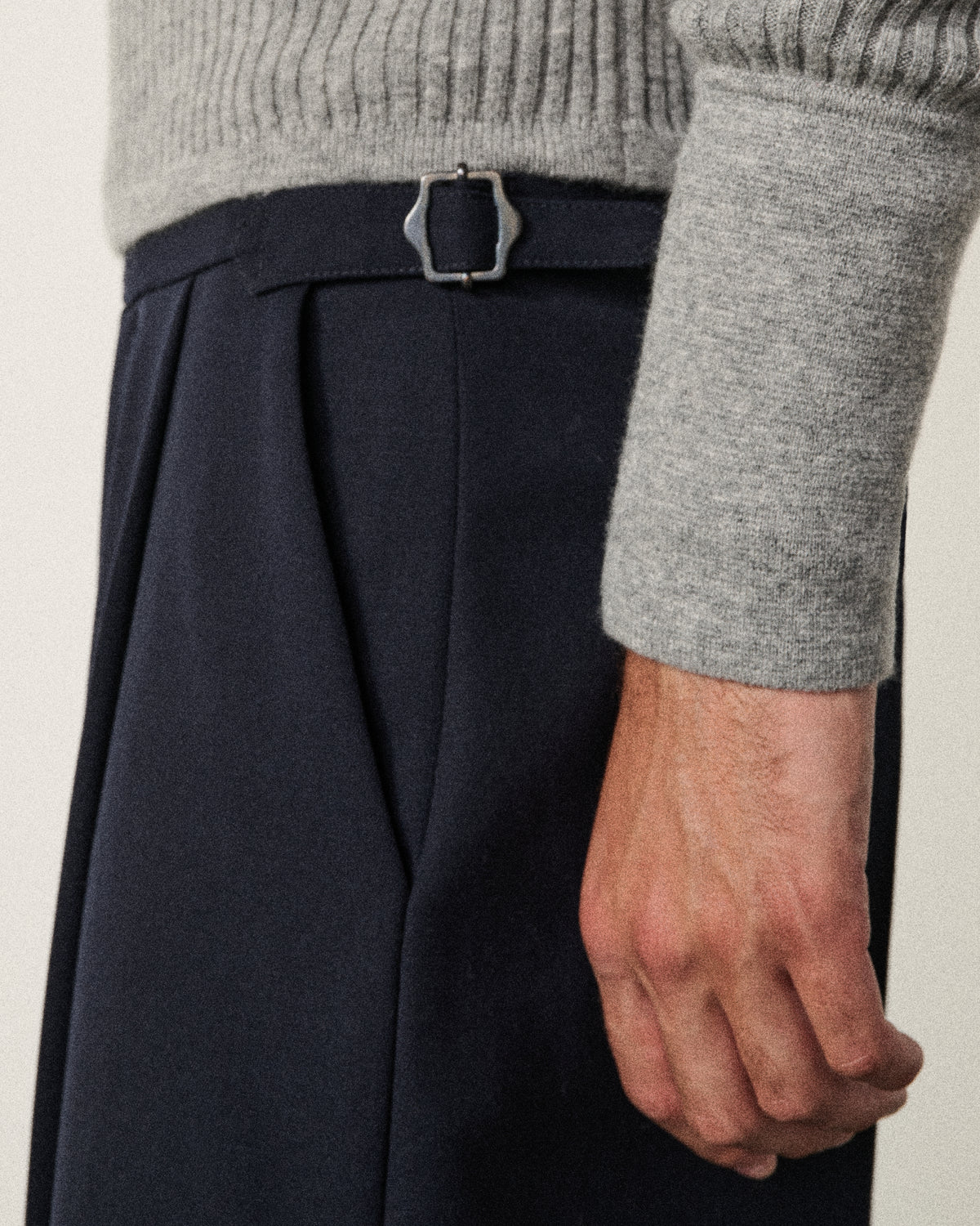 close-up of a man's hand and the navy tailored pant waist buckle
