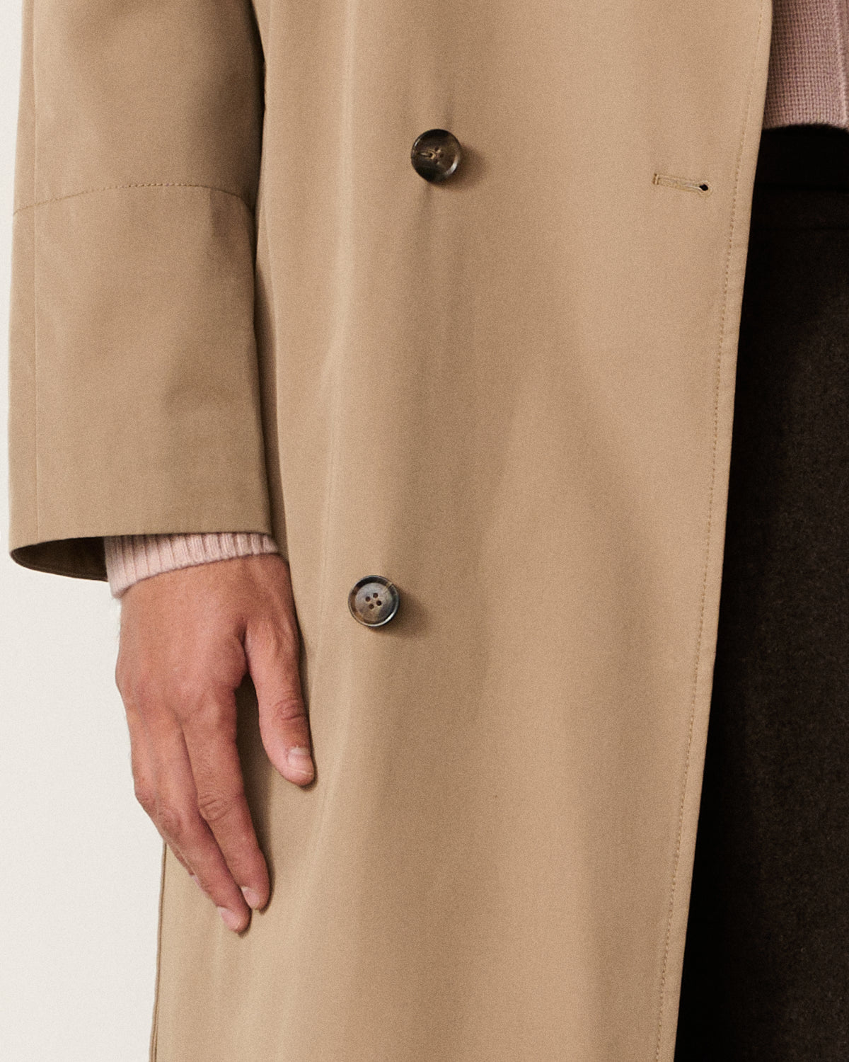 close-up of a man's hand on the trench coat buttons