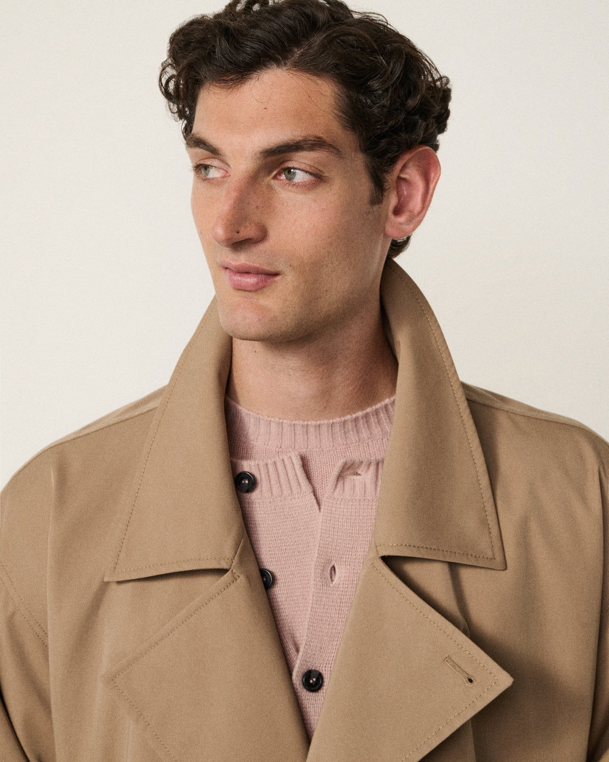 man wearing the sand trench coat over a pink sweater