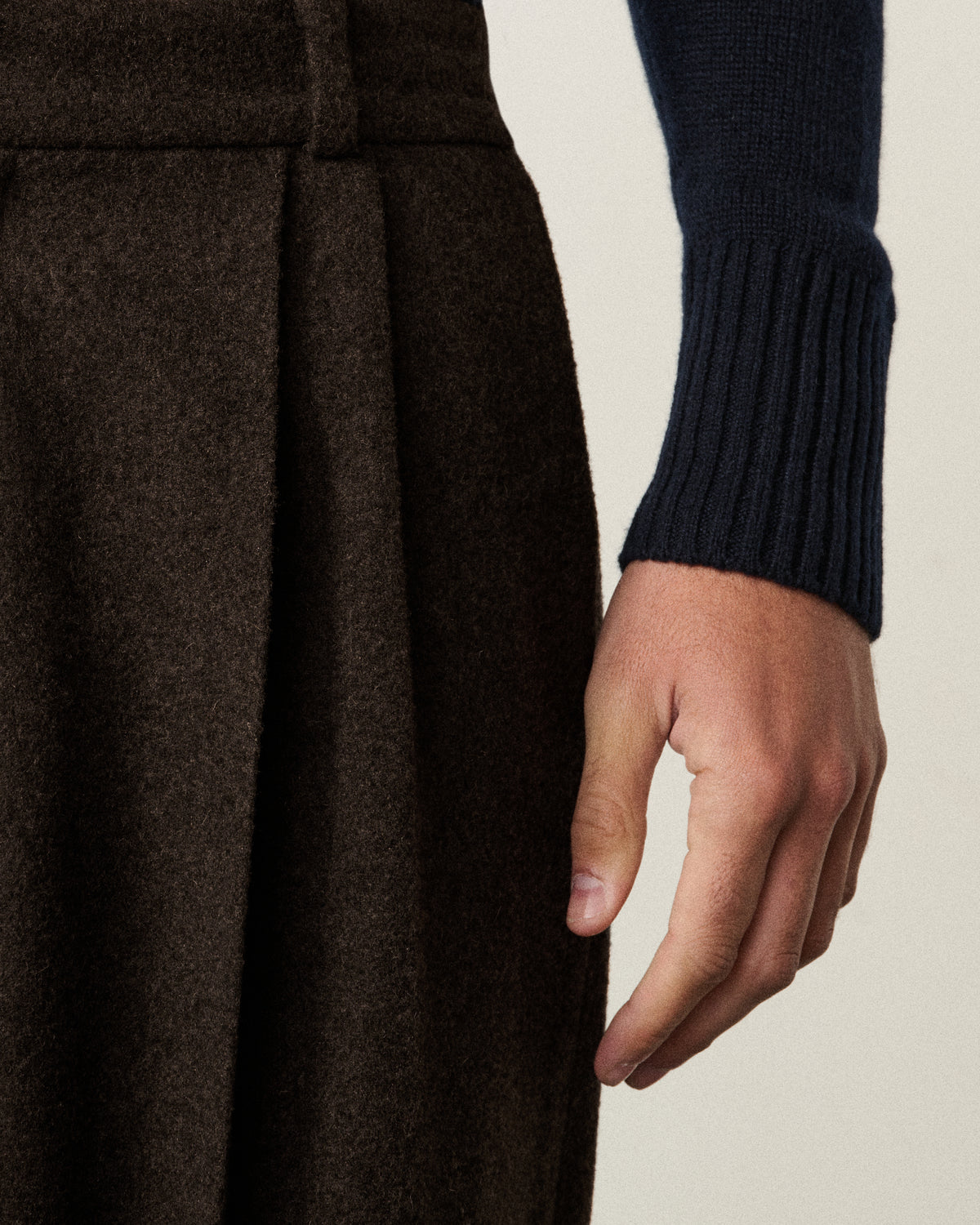 close-up of a hand on the chocolate brown pleated pants