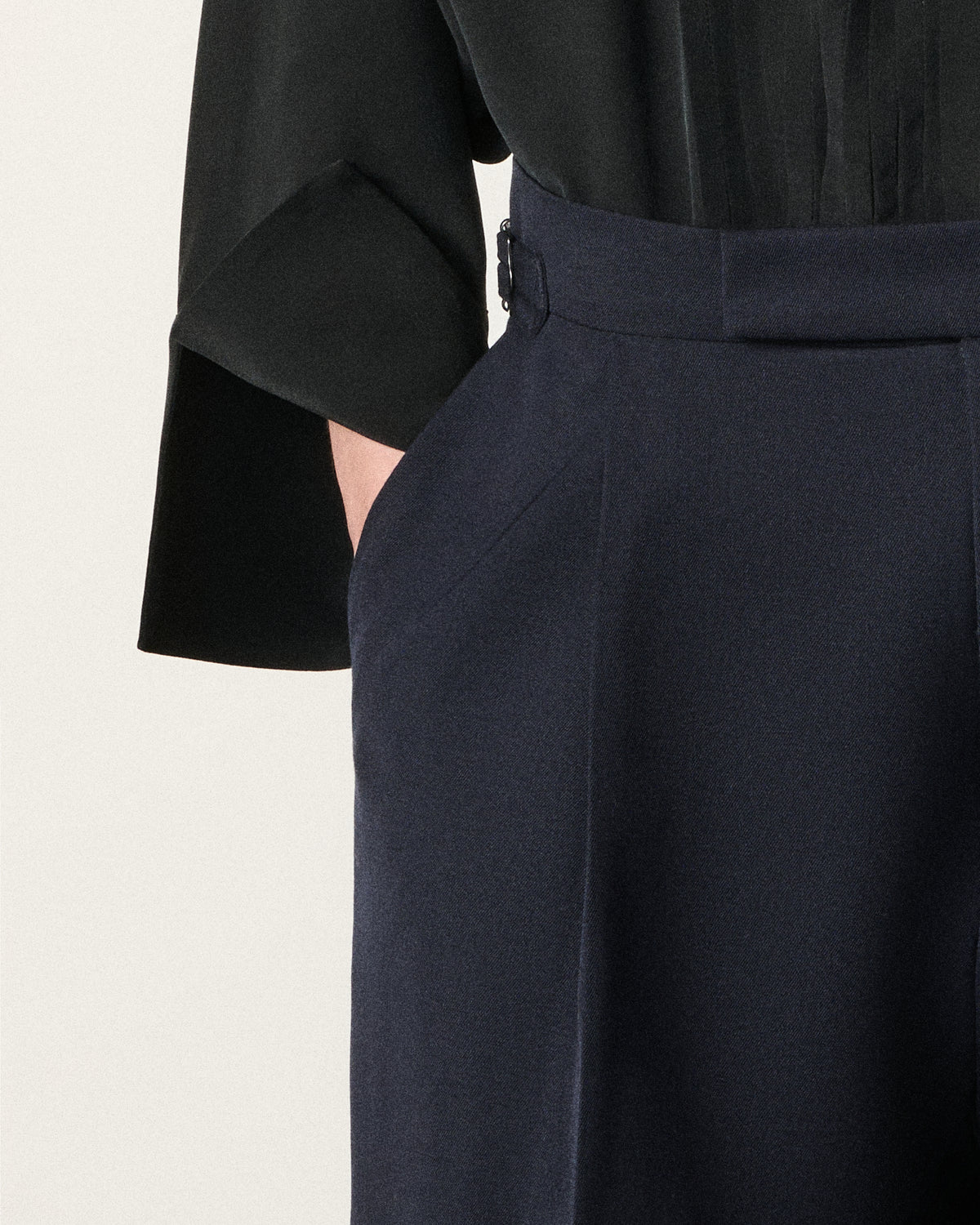 close-up of a woman's hand in the pocket of navy trousers, black tux shirt cuff