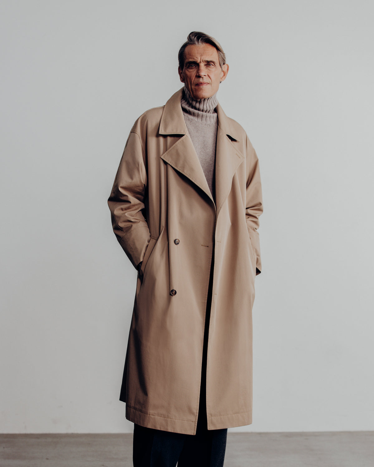 man in the sand trench coat over a grey turtleneck
