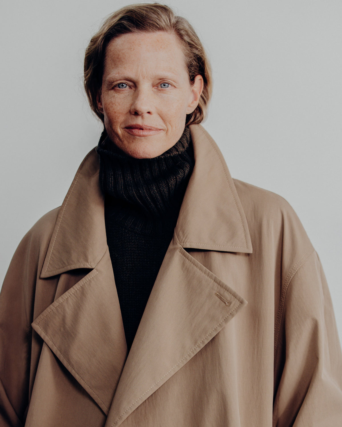 close-up of a woman's face wearing a tan coat over a dark turtle neck