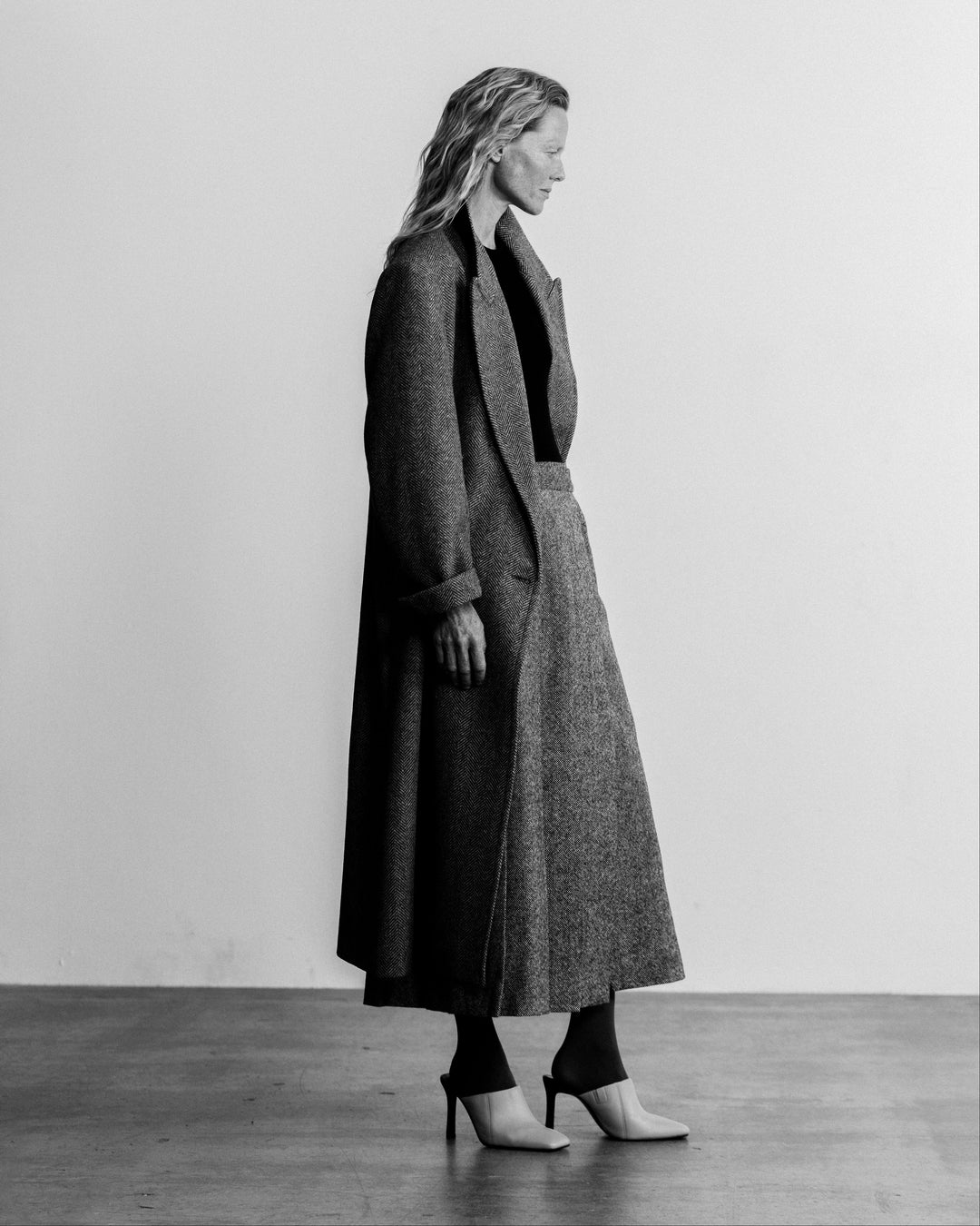 woman in a grey coat over the black and white pleated skirt, side profile