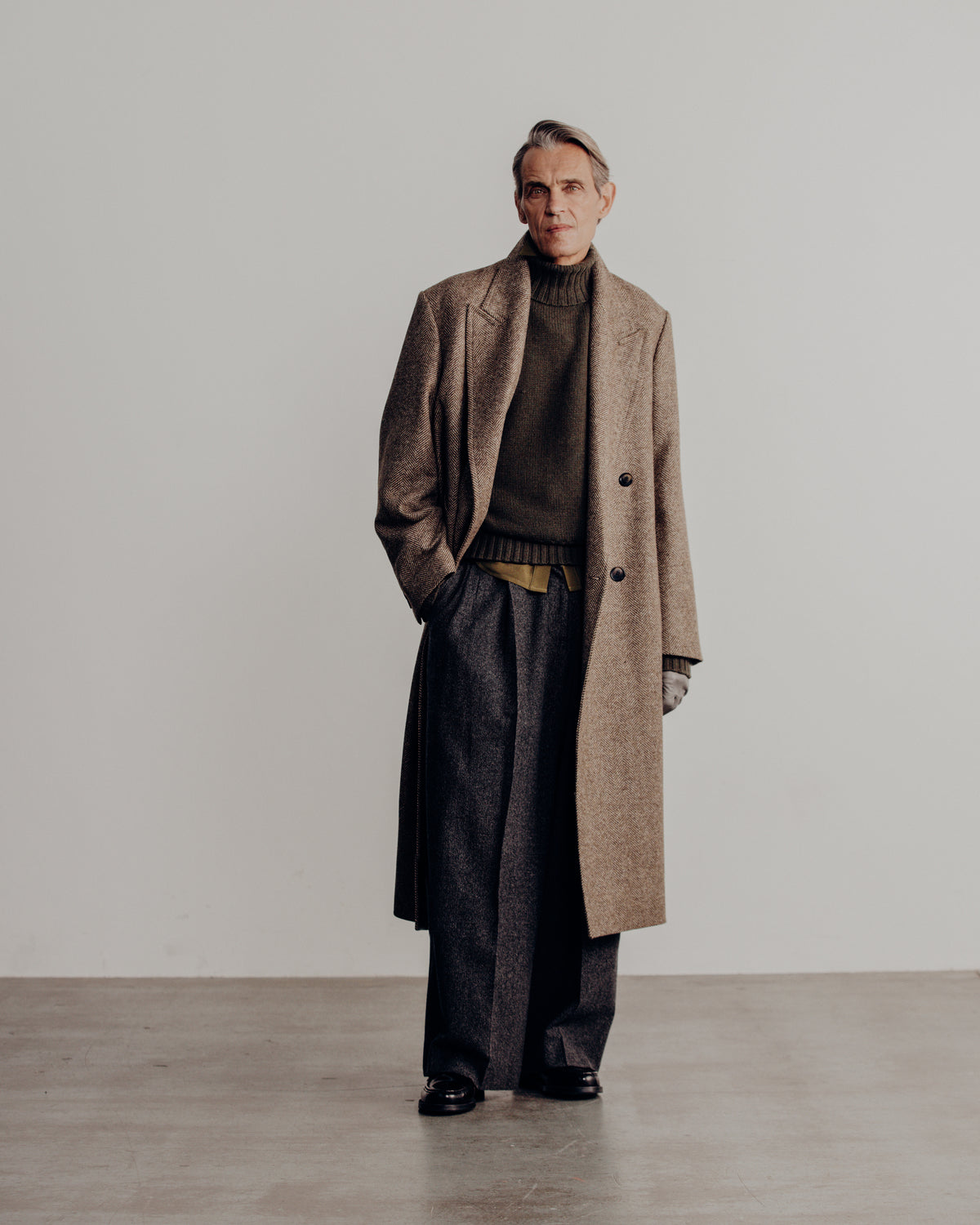man in a tan overcoat over the olive turtle neck sweater